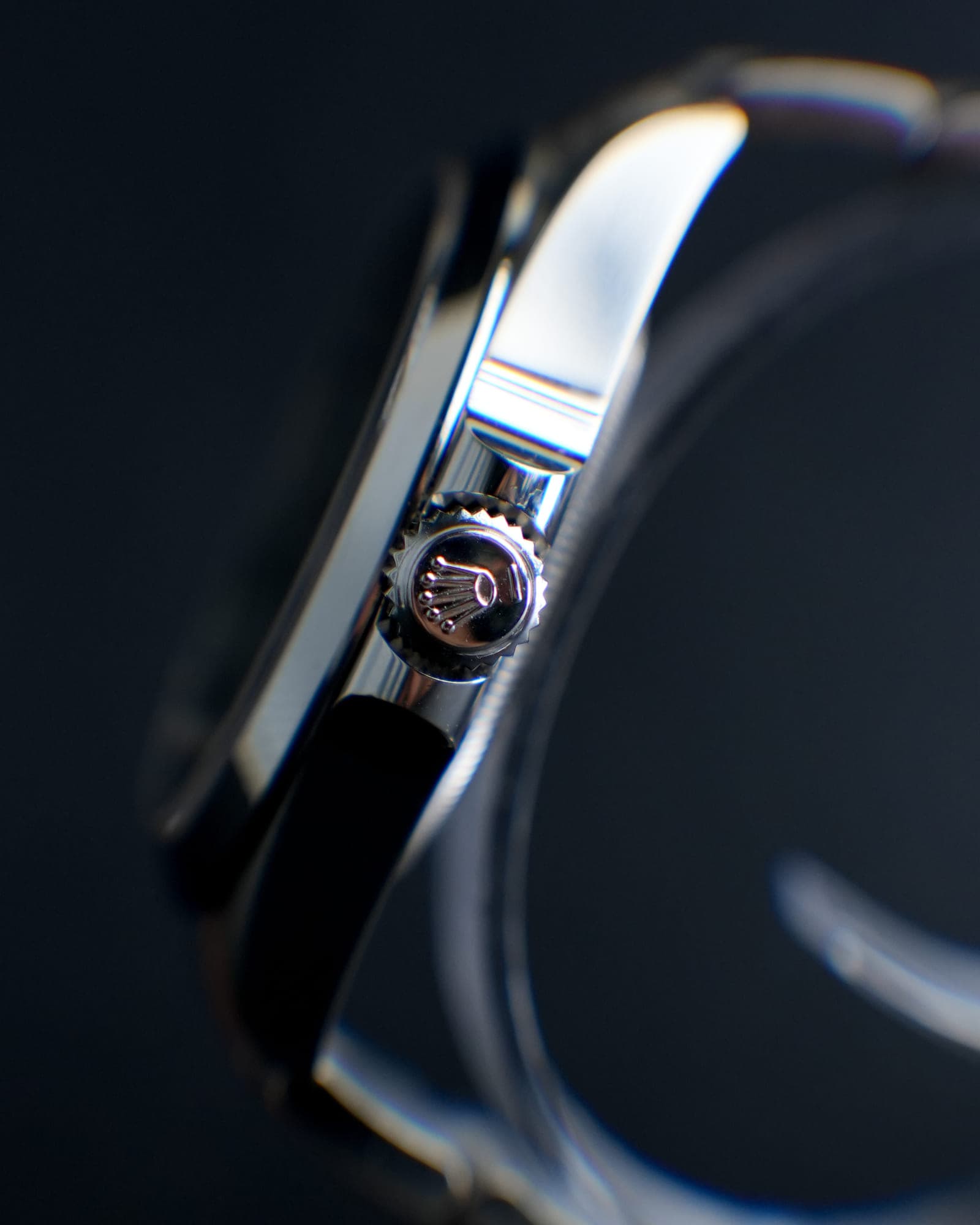 Macro detail of a Rolex Oyster case — the screw-down crown and its engraved coronet, polished bracelet catching the light