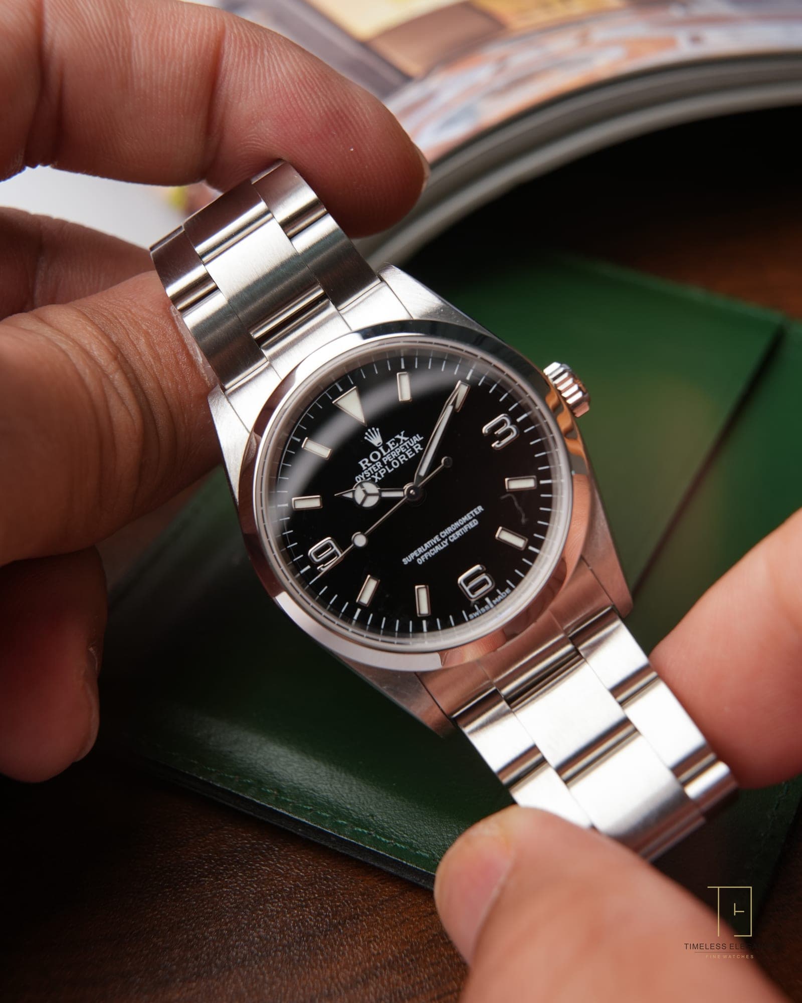 A black-dial Rolex Oyster Perpetual held in the hand, steel bracelet catching the light